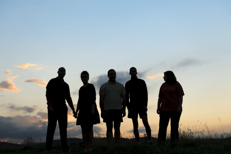 An outline of five people at sunset, with the sky behind them. They are standing on a hill.