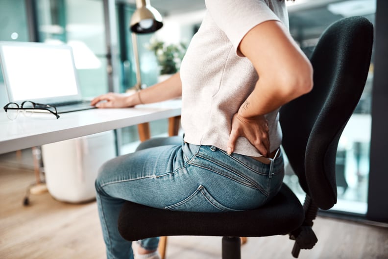 Woman experiencing lower back pain while working in an office