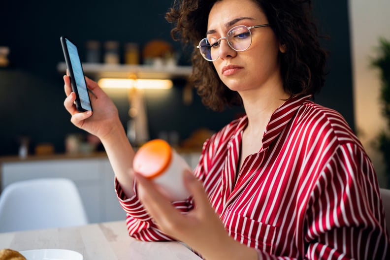 Young woman reading a medicine prescription on her smart phone while holding a pill bottle.